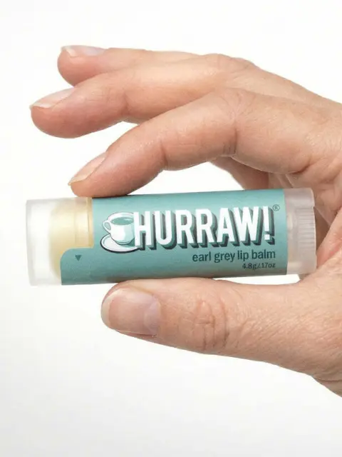 Hand holding Hurraw! Earl Grey lip balm tube.