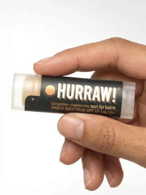 Hand holding Hurraw! tangerine chamomile sun lip balm, SPF 15, 4.8g.