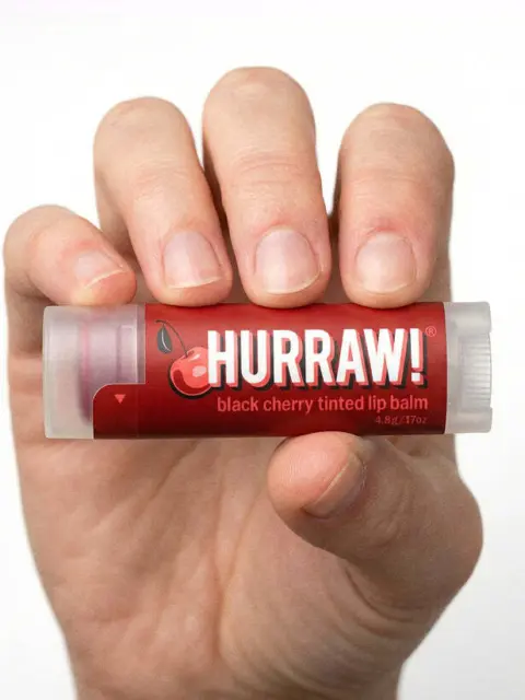 Hand holding Hurraw! black cherry tinted lip balm tube.