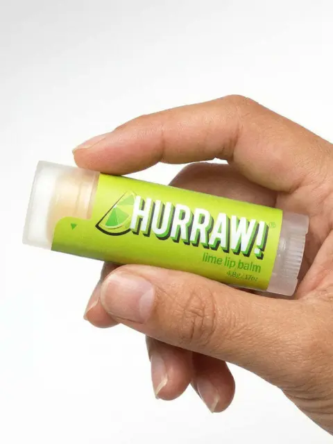 Hand holding Hurraw! lime lip balm tube.
