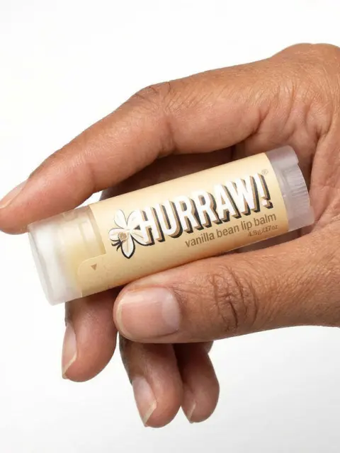 Hand holding Hurraw! vanilla bean lip balm tube.