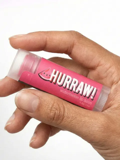 Hand holding Hurraw! watermelon lip balm tube.