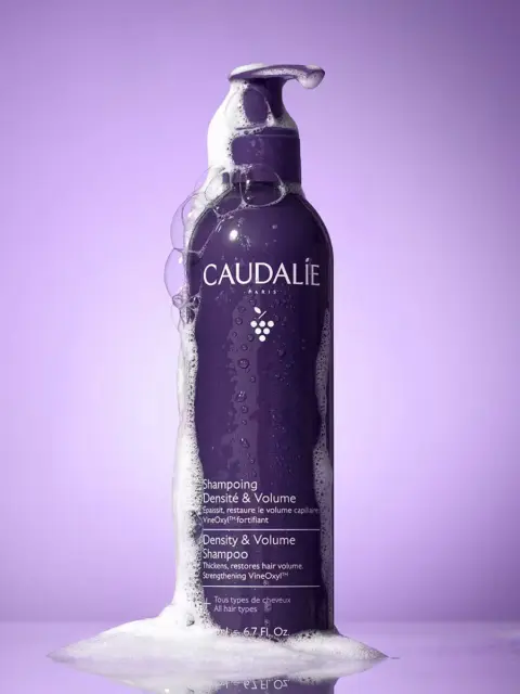 Caudalie Density & Volume Shampoo bottle with foam, purple background.