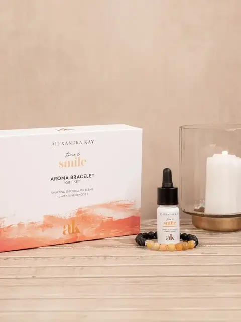 Aroma bracelet gift set with essential oil, bracelet, and candle on wooden surface.