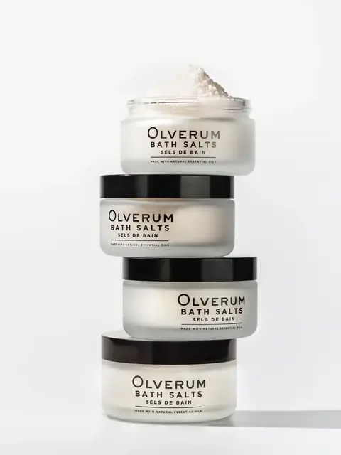 Stack of four Olverum bath salts jars with black lids on a white background.