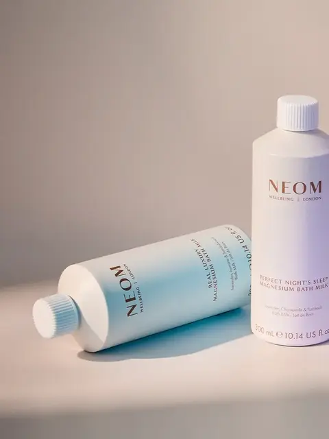 Two NEOM magnesium bath milk bottles on a light surface.