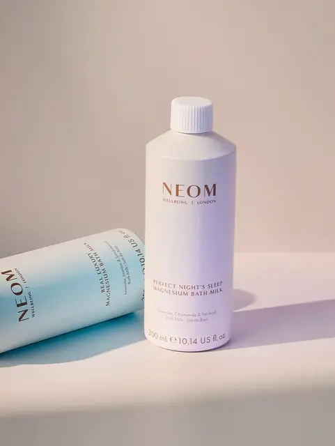 Two NEOM magnesium bath milk bottles on a light surface.