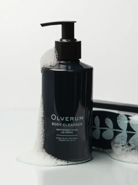 Dark bottle of Olverum body cleanser with foam, next to a matching tube.