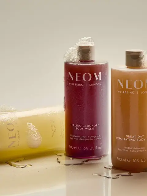Three NEOM body wash bottles with foam, labelled "Feeling Grounded" and "Great Day".