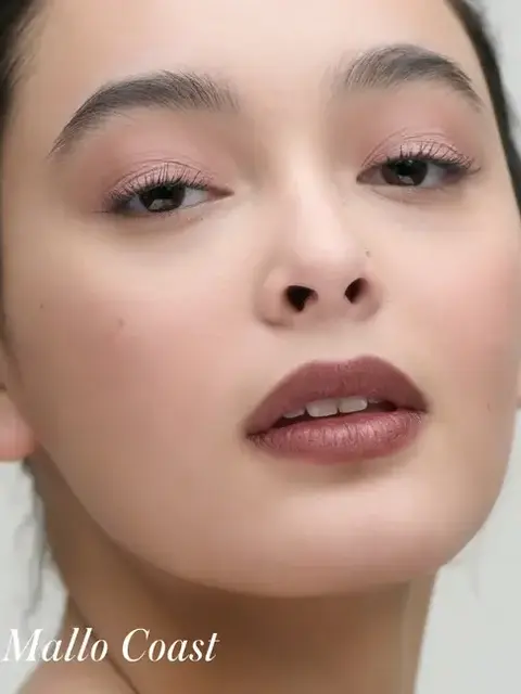 Close-up of a person with natural makeup. Text: "Mallo Coast".