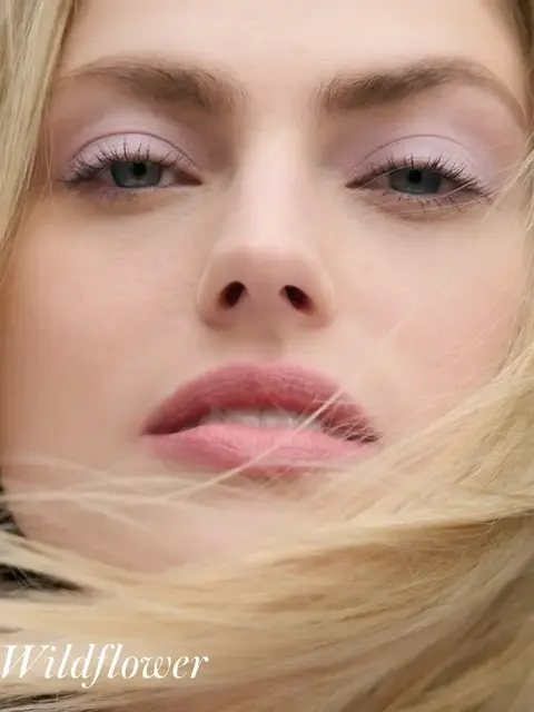 Close-up of a woman's face with pink eyeshadow and lipstick. Text: "Wildflower".
