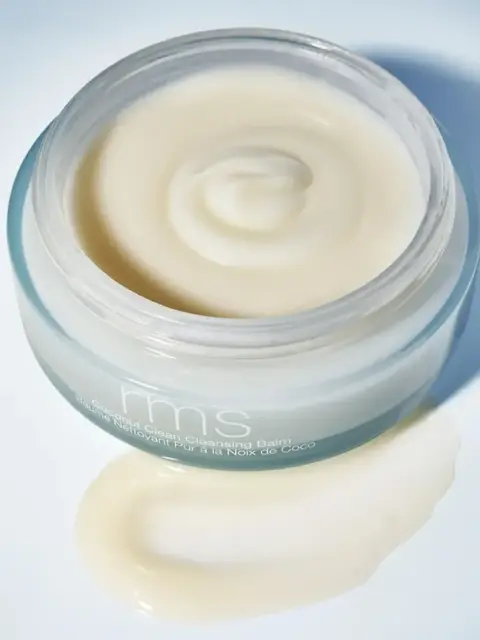Open jar of rms coconut cleansing balm with some balm spilled on surface.