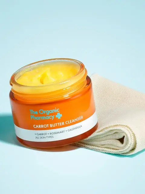Orange jar of Carrot Butter Cleanser with cloth on blue background.