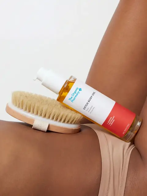 Body oil bottle and brush on a person's leg in beige underwear.
