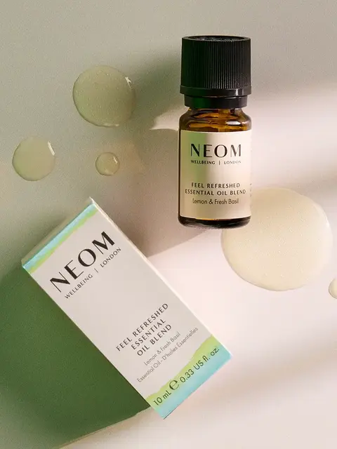 NEOM Feel Refreshed essential oil blend bottle and box on a light surface with oil droplets.