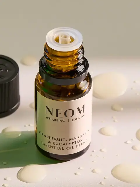 Open bottle of NEOM essential oil with drops on a surface.