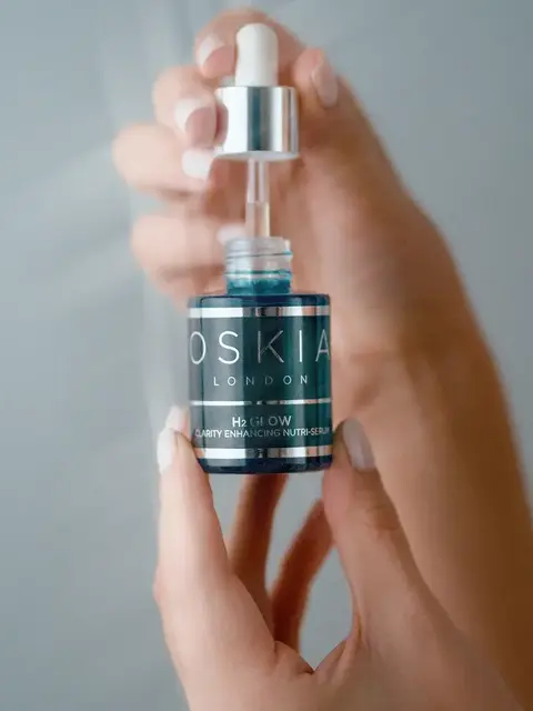 Hands holding Oskia London H2Glow serum with dropper.