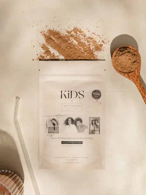 KiDS wholefood nutrition powder with spoon, straw, and spilled powder on a light surface.
