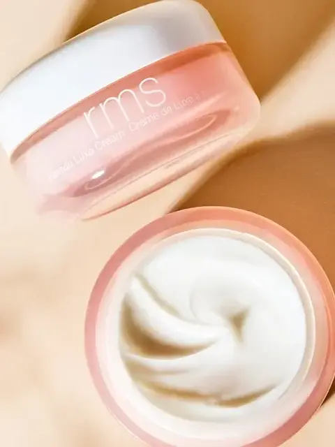 Open jar of RMS cream with white lid and smooth cream inside, on a beige background.