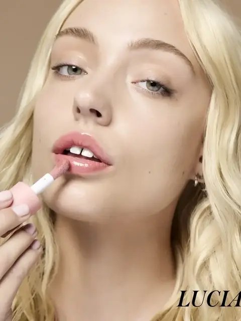 Woman applying pink lipstick, blonde hair, text "LUCIA" in corner.