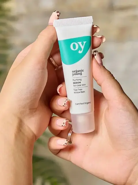 Hands holding a tube of "oy" purifying serum for clear skin.