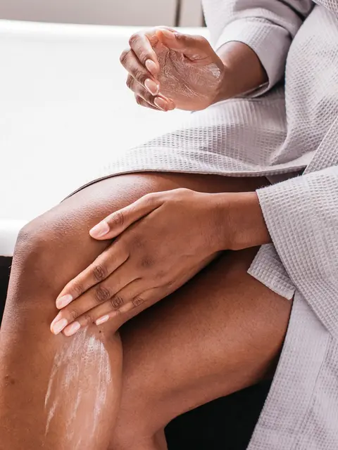 Person applying lotion to leg while wearing a grey robe.