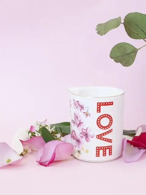 White jug with "LOVE" text, floral design, surrounded by pink petals on a pink background.