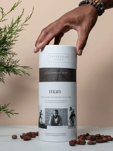 Hand reaching for Supernova Living nutrition drink container on table with cocoa beans.