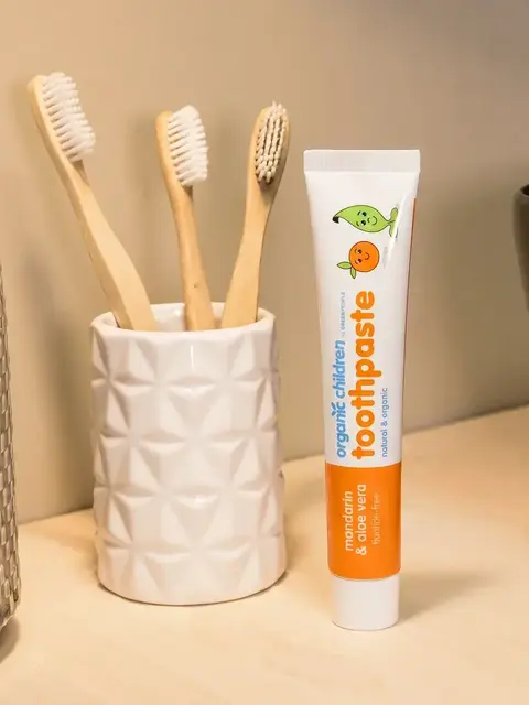 Tube of organic children's toothpaste beside bamboo toothbrushes in a holder.