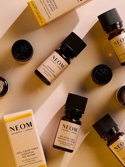 Neom essential oil bottles and packaging on a beige surface.
