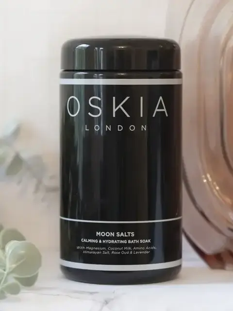 Oskia London Moon Salts jar on marble surface with eucalyptus leaves.