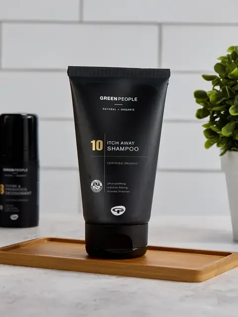 Green People Itch Away Shampoo tube on a wooden tray, with a plant and other products nearby.