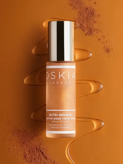 Oskia London Nutri-Bronze serum bottle on bronze background with liquid and powder accents.