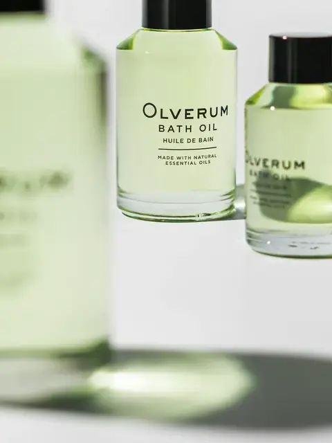 Olverum Bath Oil bottles with green liquid and black caps. Text: "Made with natural essential oils".