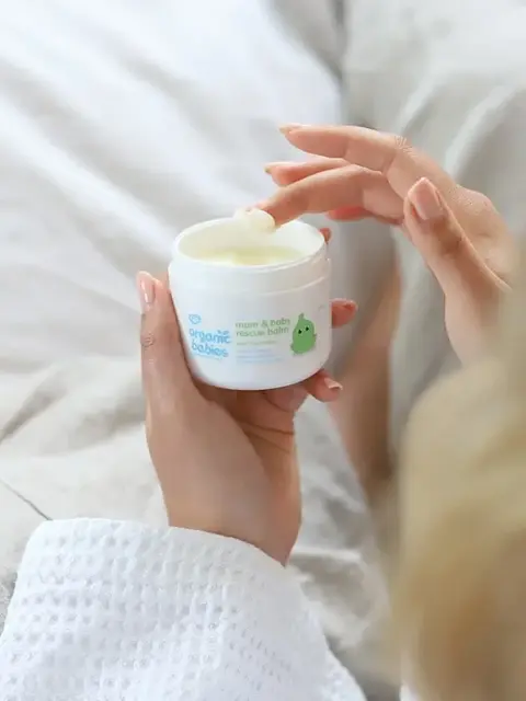 Hand applying Organic Babies mum & baby rescue balm from a white jar.