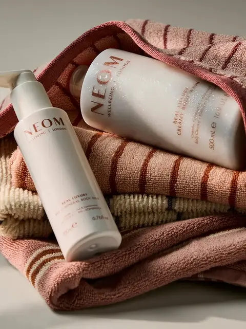 NEOM body lotion and cream on folded striped towels.