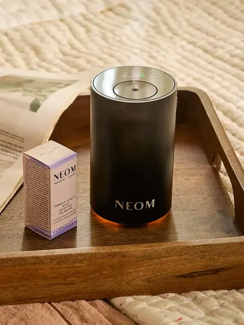 NEOM diffuser and oil box on a wooden tray with a cup and newspaper.