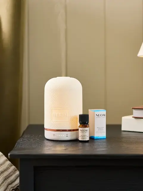 Diffuser and essential oil on bedside table with lamp and books.