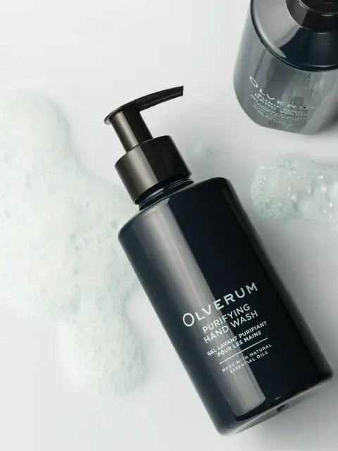 Dark bottle of Olverum Purifying Hand Wash with foam on a white surface.