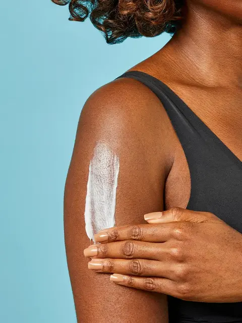 Woman applying lotion to her arm against a blue background.
