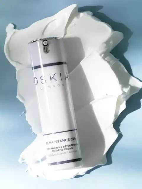 Oskia Renaissance 360 cream bottle on white cream smear, blue background.