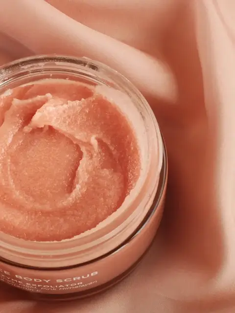Open jar of pink body scrub on a silky pink fabric background.