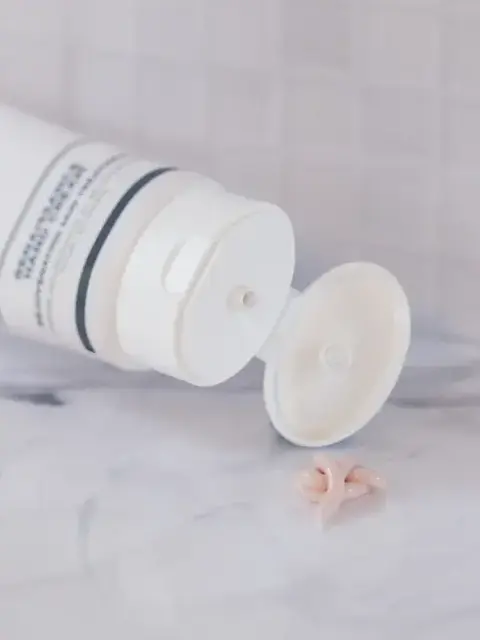 White skincare tube open on marble surface, cream squeezed out.