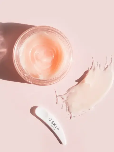 Open jar of pink cream with a white spatula labelled "O.S.K.I.A London" on a pink background.