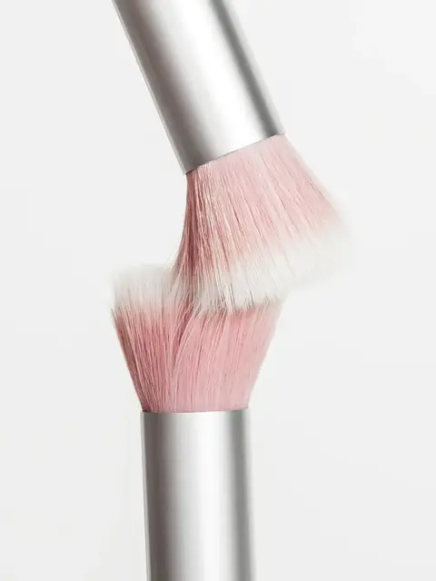Two pink makeup brushes with silver handles touching bristles.