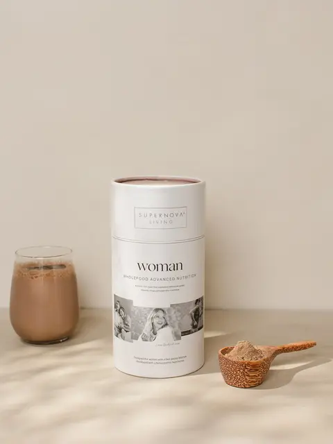 Supernova Living Woman supplement with a glass of chocolate drink and a wooden scoop of powder.