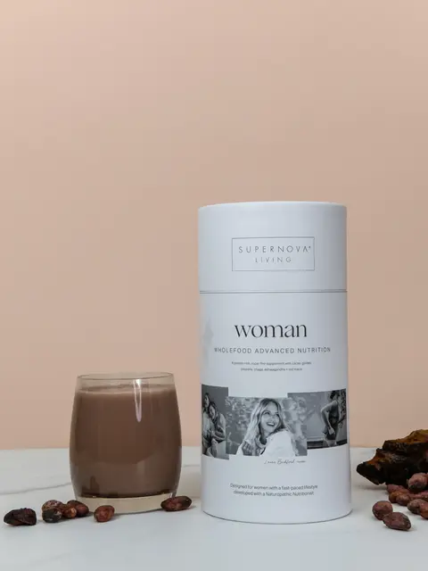 Supernova Living Woman nutrition powder with a glass of chocolate drink on a marble surface.