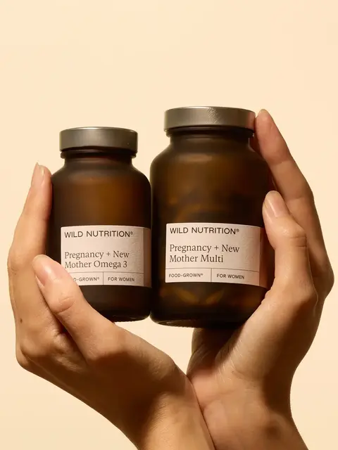 Two hands holding Wild Nutrition supplements for pregnancy and new mothers.