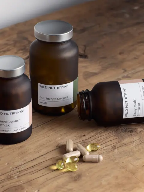 Three brown supplement bottles on a wooden table with capsules and softgels.