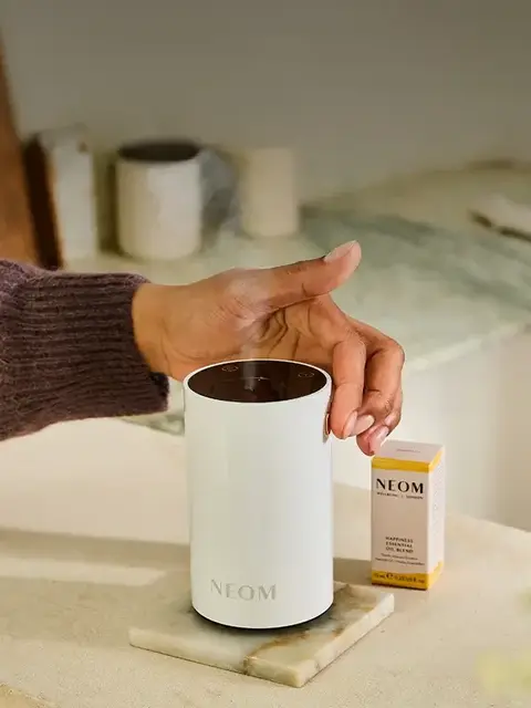 Hand adjusting a NEOM diffuser on a marble surface, with a NEOM oil blend box nearby.